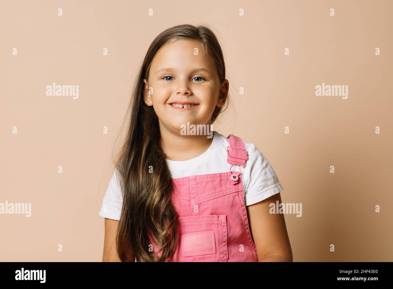 Portrait Foto von weiblichen Kind mit hellen leuchtenden Augen und ruhig glücklich breiten Lächeln mit Zähnen Blick auf die Kamera trägt leuchtend rosa Jumpsuit und weiß t Stockfoto