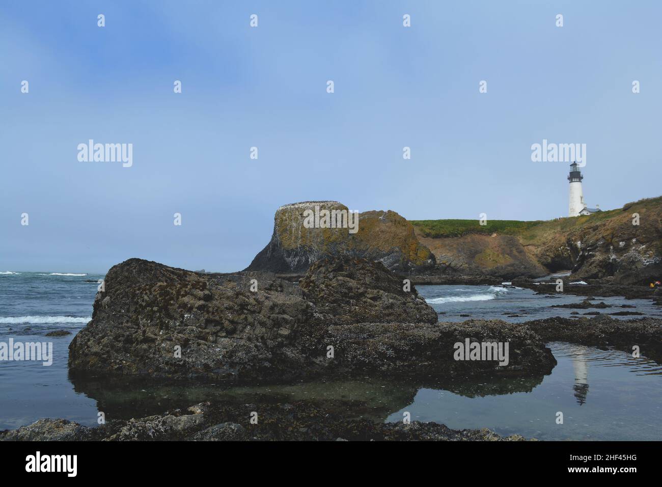 An einem leicht nebligen Tag an der felsigen Küste von Oregon spiegelt sich ein Leuchtturm in einem Tidepool wider Stockfoto