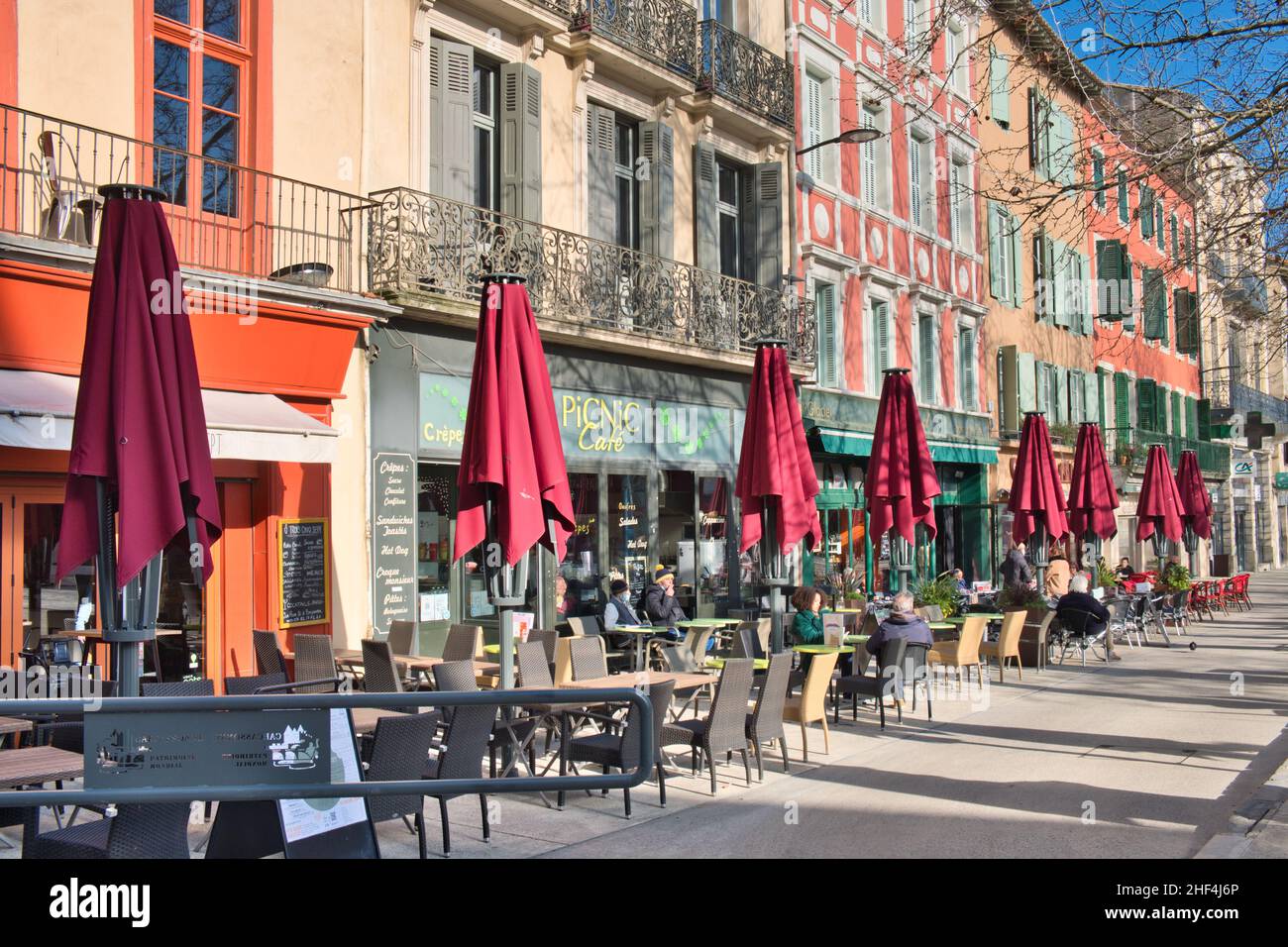 Place Carnot, Carcassonne Aude France 01.13.22 strahlender Wintertag. Cafés mit Sitzgelegenheiten im Freien. Reihe roter Parasols. Elegante, farbenfrohe Gebäude Stockfoto