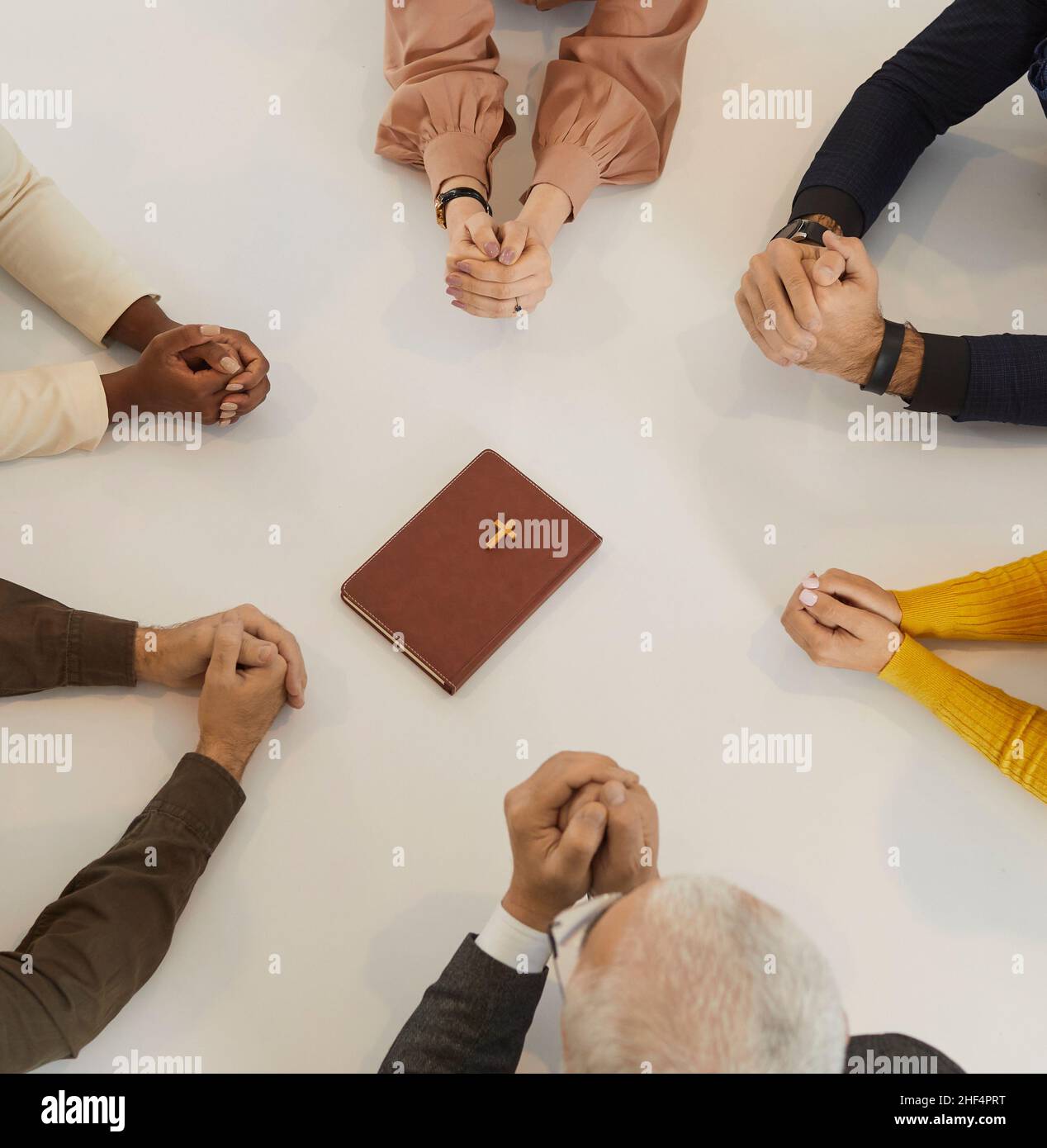 Verschiedene Menschen, die mit der Heiligen Bibel um den Tisch sitzen und gemeinsam zu Gott beten Stockfoto