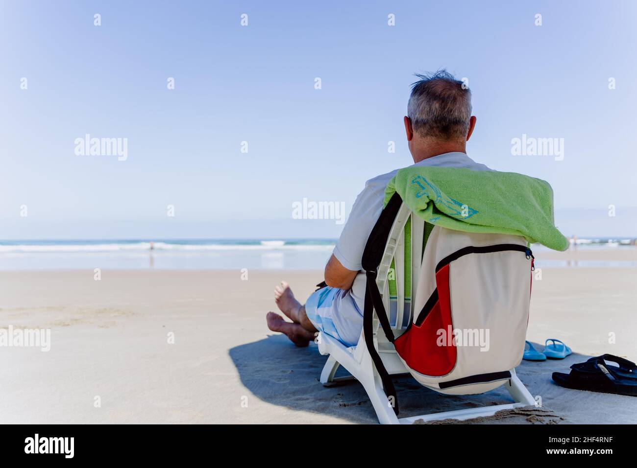 Alter Mann, der am Strand sitzt Stockfoto