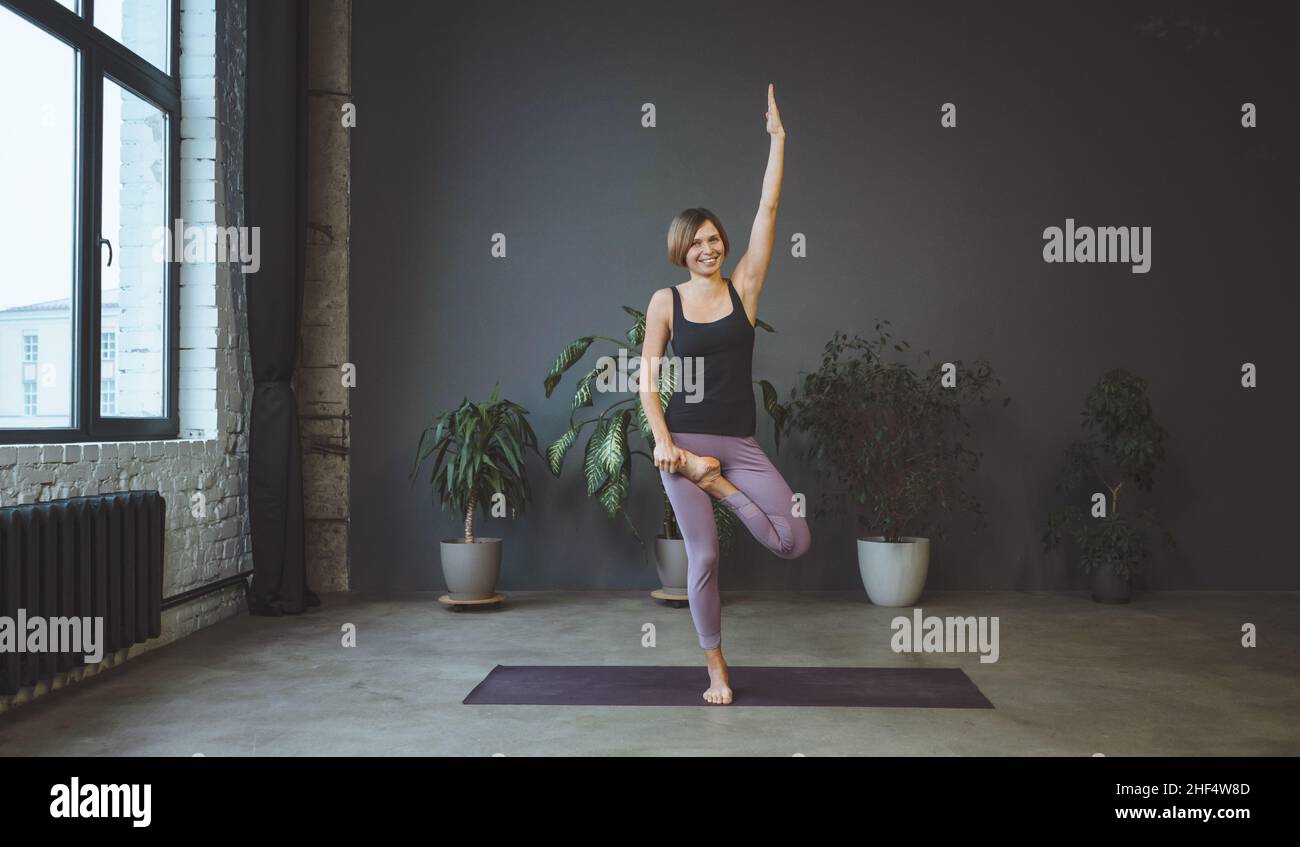 Lonely Woman in Sportswear macht Side Plank in einem geräumigen Yoga Studio. Die Sportliche Frau Praktiziert Hatha Yoga. Volle Länge. Grauer Hintergrund. Hochwertige Fotos Stockfoto