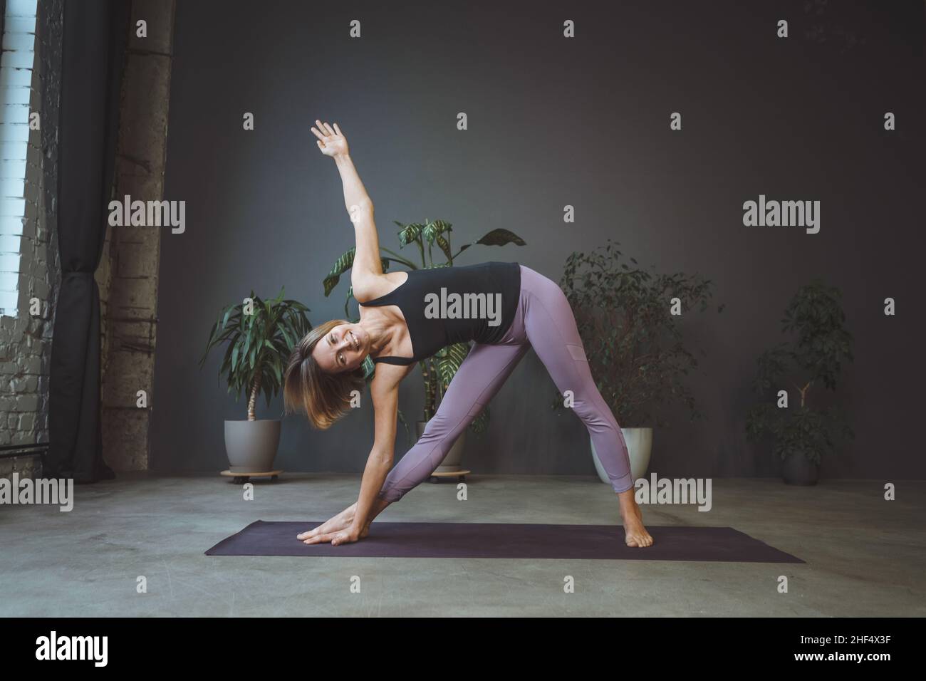 Einsame Frau in Sportswear beim Plank in einer Wohnung in einer Metropole. Die Sportliche Frau Praktiziert Hatha Yoga. Volle Länge. Grauer Hintergrund. Hochwertige Fotos Stockfoto