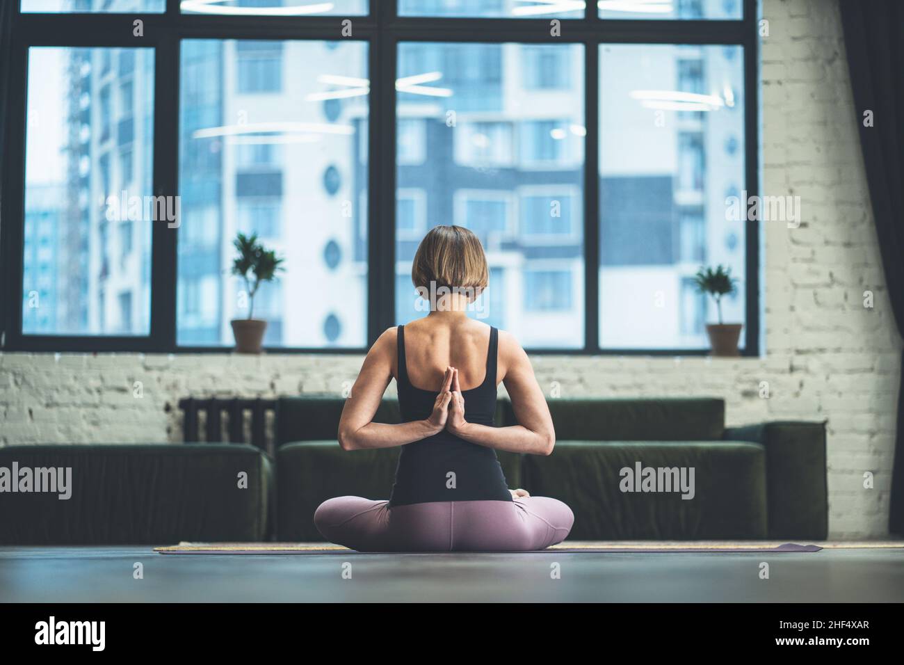 Frau, die in Lotus-Pose sitzt und mit offenen Händen meditiert. Yoga-Frau praktiziert Yoga-Meditationsübung auf der Matte in ihrem Wohnzimmer zu Hause. Nahaufnahme. Hochwertige Fotos Stockfoto