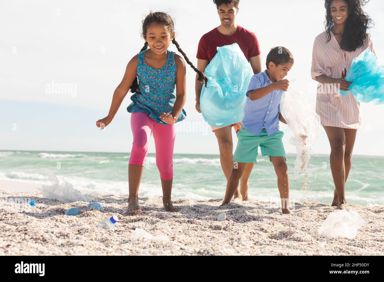 Glückliche, verantwortungsvolle multirassische Familie, die am sonnigen Tag Plastikmüll aus Sand am Strand sammelt Stockfoto