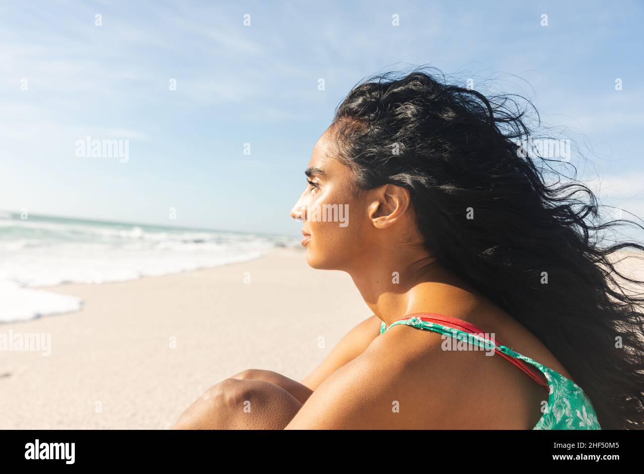 Seitenansicht einer nachdenklichen jungen Birazialfrau mit langen schwarzen Haaren und Blick auf den Strand Stockfoto