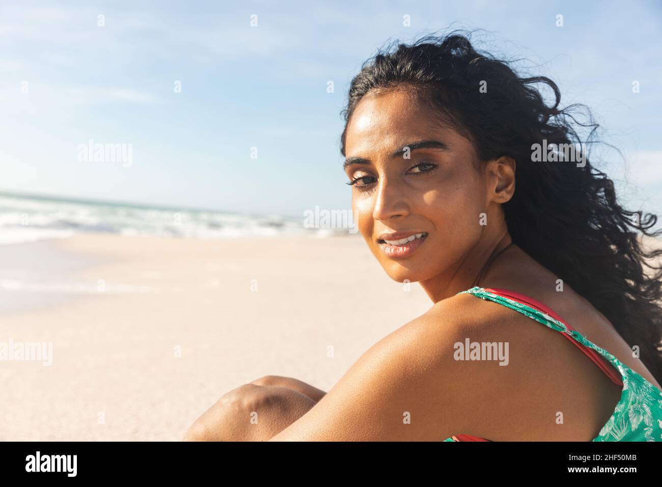 Seitenansicht Porträt einer jungen Birazialfrau mit langen schwarzen Haaren, die an sonnigen Tagen am Strand sitzt Stockfoto