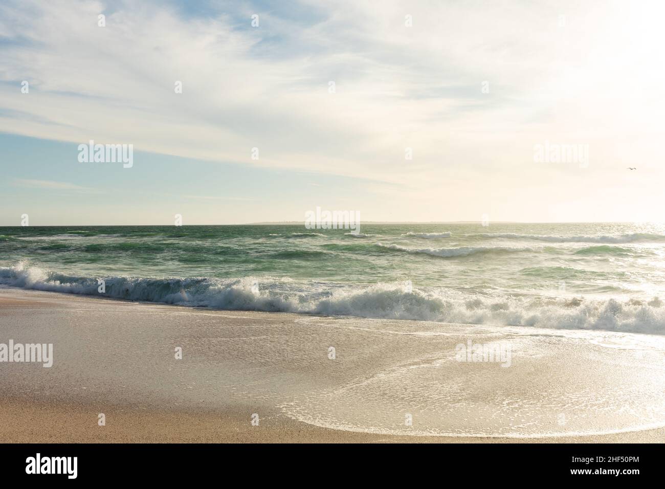 Am Strand plätschern Meereswellen gegen den Himmel und Wolken am sonnigen Tag Stockfoto
