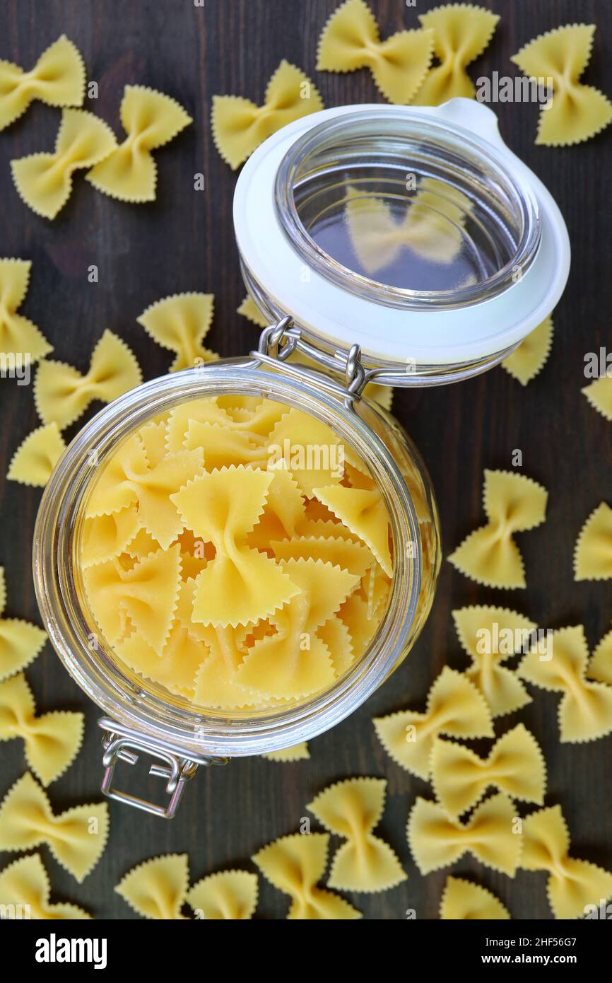 Draufsicht auf getrocknete Farfalle Pasta in einem geöffneten Glasglas mit einigen verstreuten Stockfoto