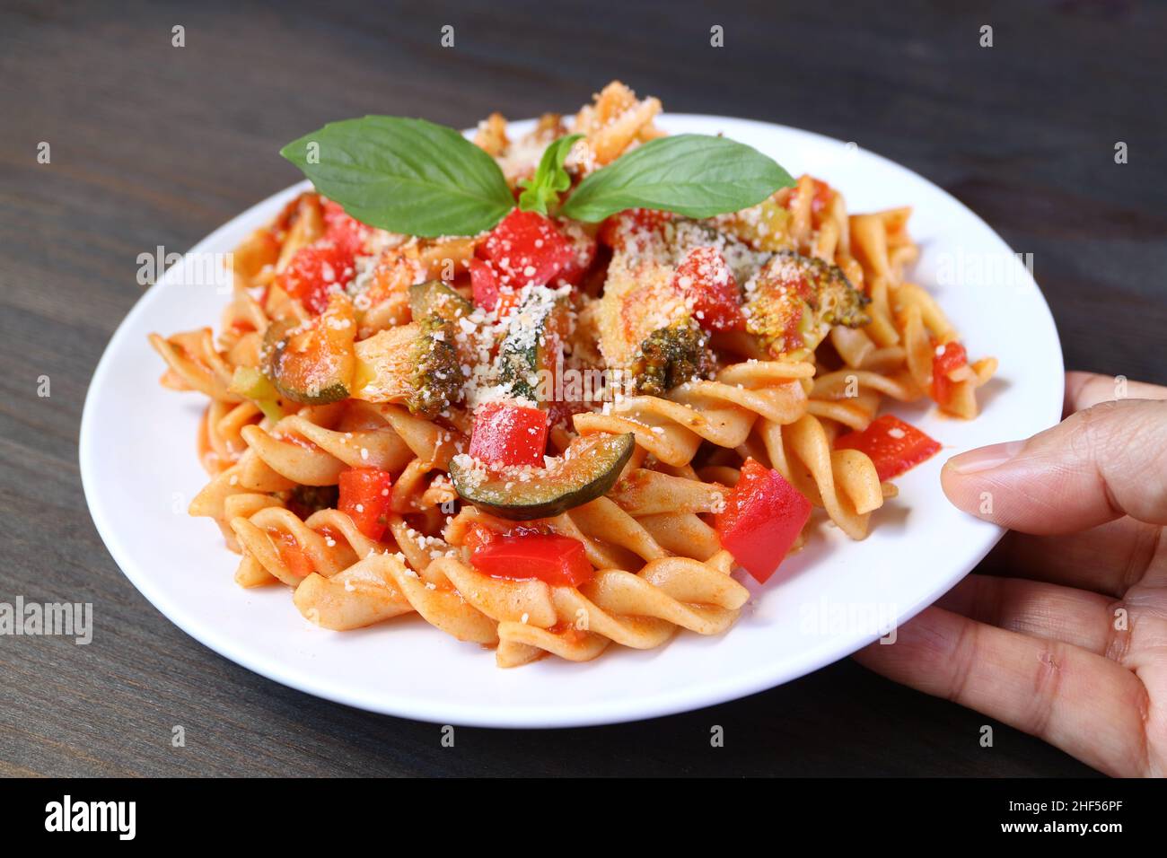 Hand eine Platte aus köstlichen Vollkornnudeln in Tomatensauce auf Holztisch Stockfoto
