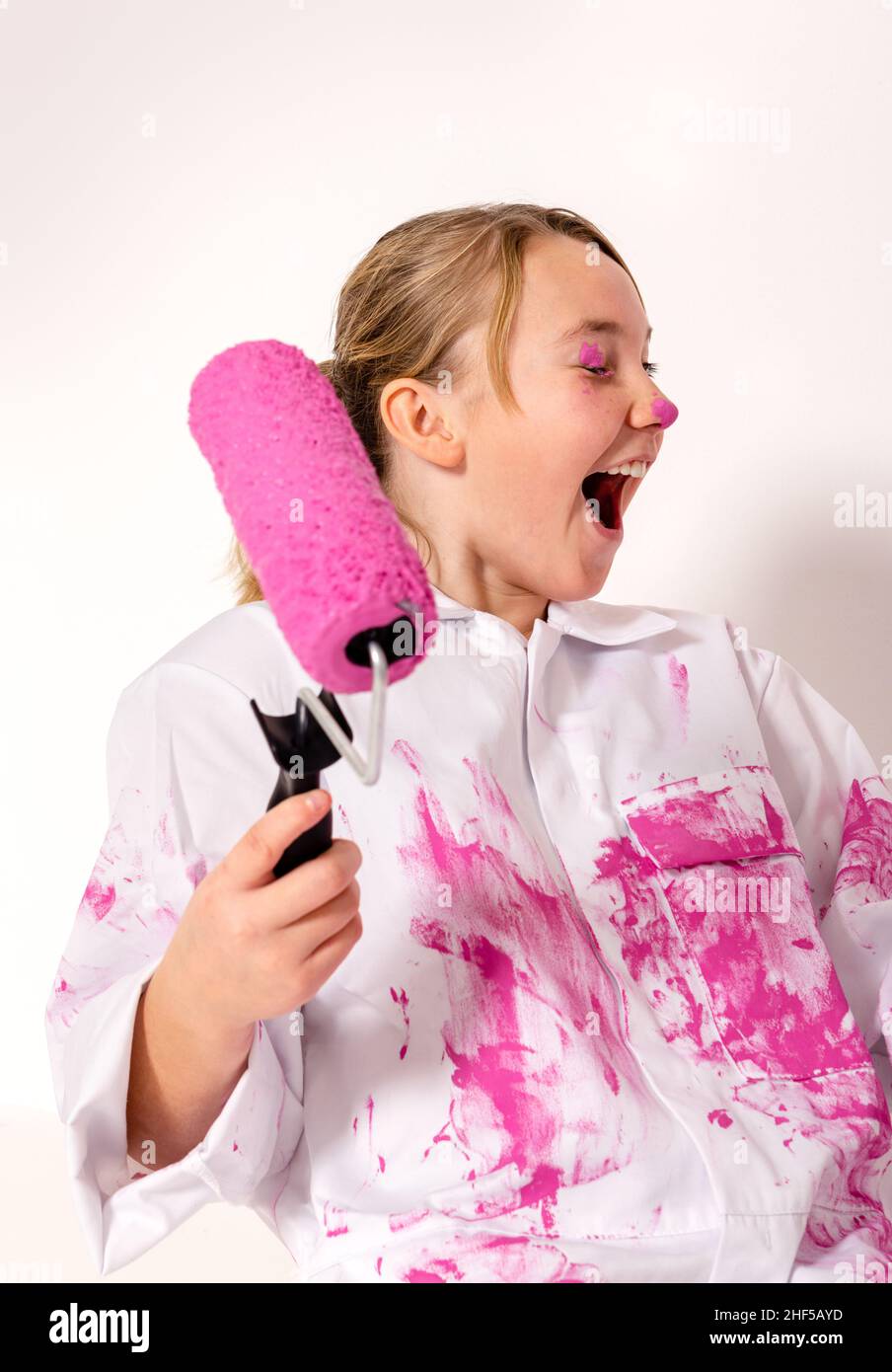 Junges Mädchen mit einer mit rosa Farbe gefüllten Walze. Sie hat Farbe auf ihrem Augenlid und lacht glücklich. Stockfoto
