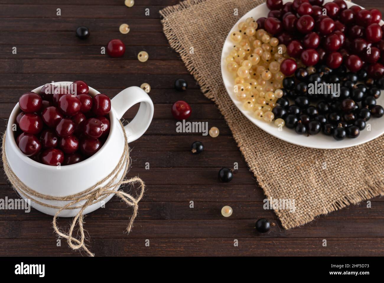 Auf einem Holztisch stehen verschiedene Beeren aus Kirschen, weißen und schwarzen Johannisbeeren. Horizontales Foto. Stockfoto