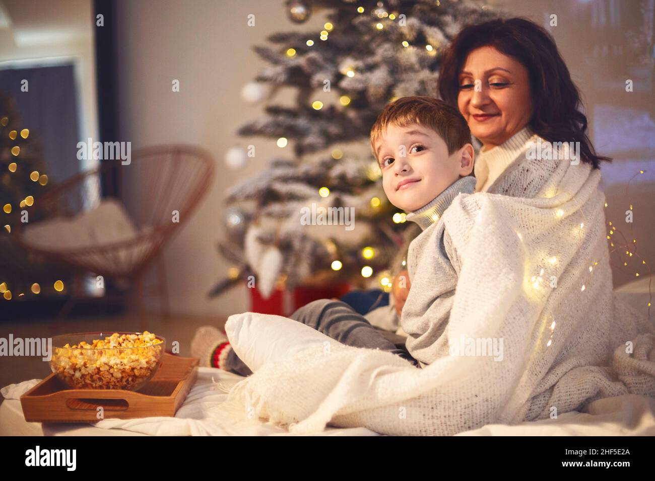 Familientraditionen. Mutter und kleiner Junge Sohn schauen Weihnachtsfilm oder tv mit Popcorn zu Hause, sitzen unter der Decke in gemütlichen Zimmer mit Weihnachtsbaum du Stockfoto