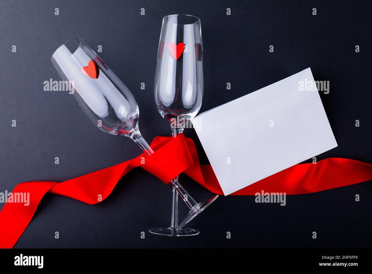 Leere Sektflöten, die mit einem roten Band an einem Umschlag mit Kopierfläche auf grauem Hintergrund gebunden sind Stockfoto