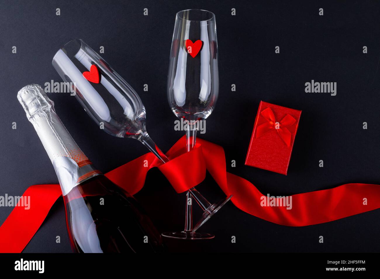 Sektflöten mit rotem Band durch Geschenkbox und Flasche auf grauem Hintergrund gebunden, Kopierraum Stockfoto