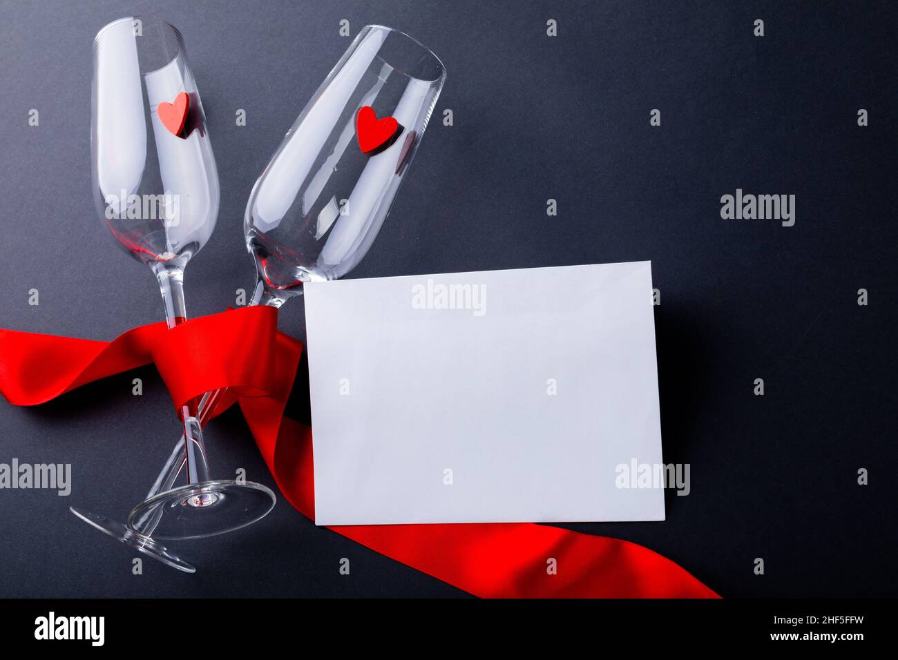 Sektflöten mit rotem Band durch leeren Umschlag isoliert auf grauem Hintergrund gebunden, kopieren Raum Stockfoto