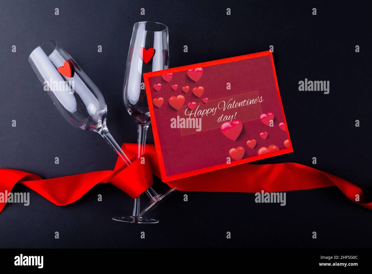 Valentinstags-Geschenkkarte mit Sektflöten, eingewickelt mit rotem Band auf schwarzem Tisch mit Platz zum Kopieren Stockfoto