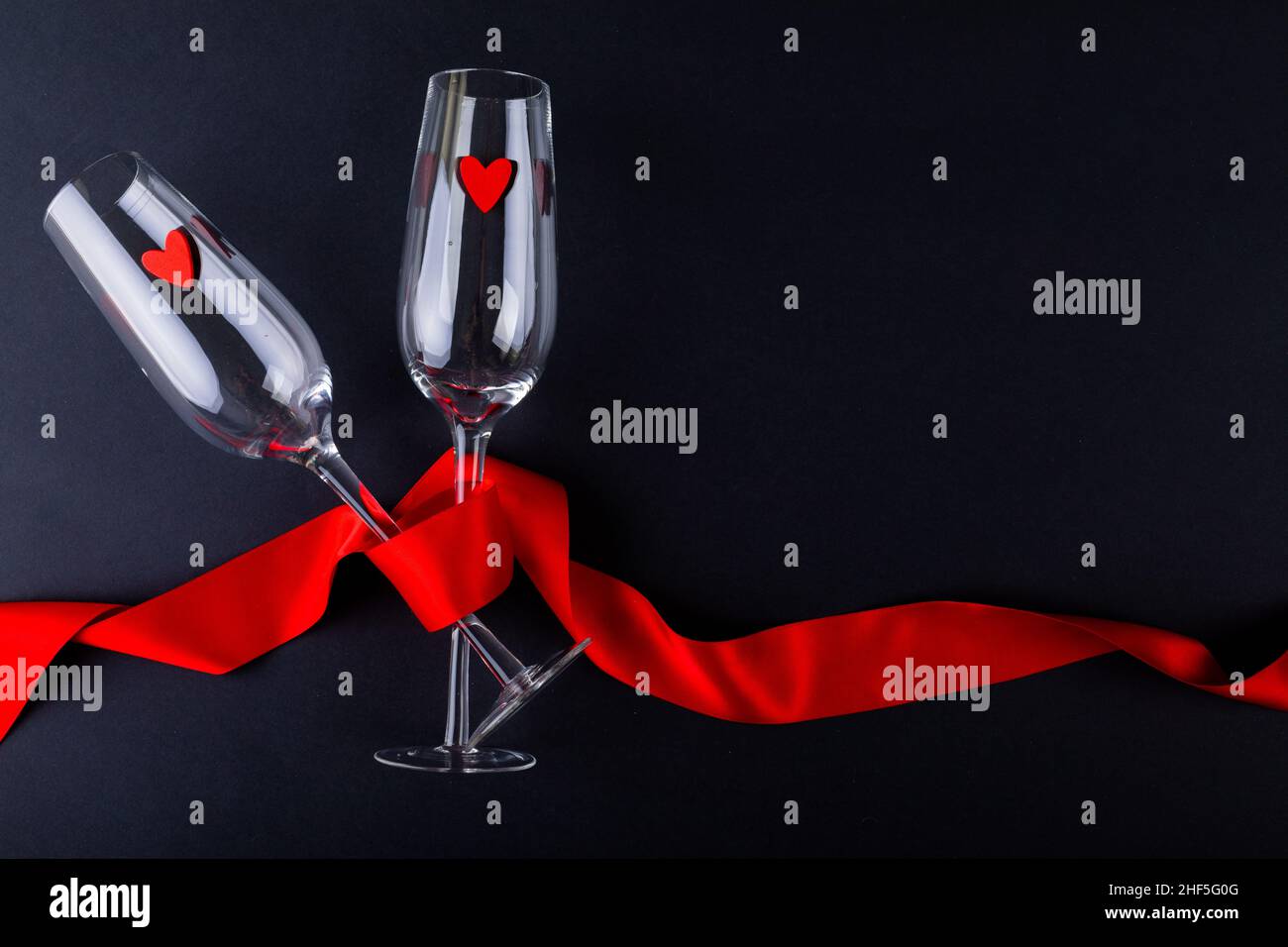Herzformen in leeren Champagnerflöten, umhüllt mit rotem Band, durch Copy Space auf schwarzem Hintergrund Stockfoto