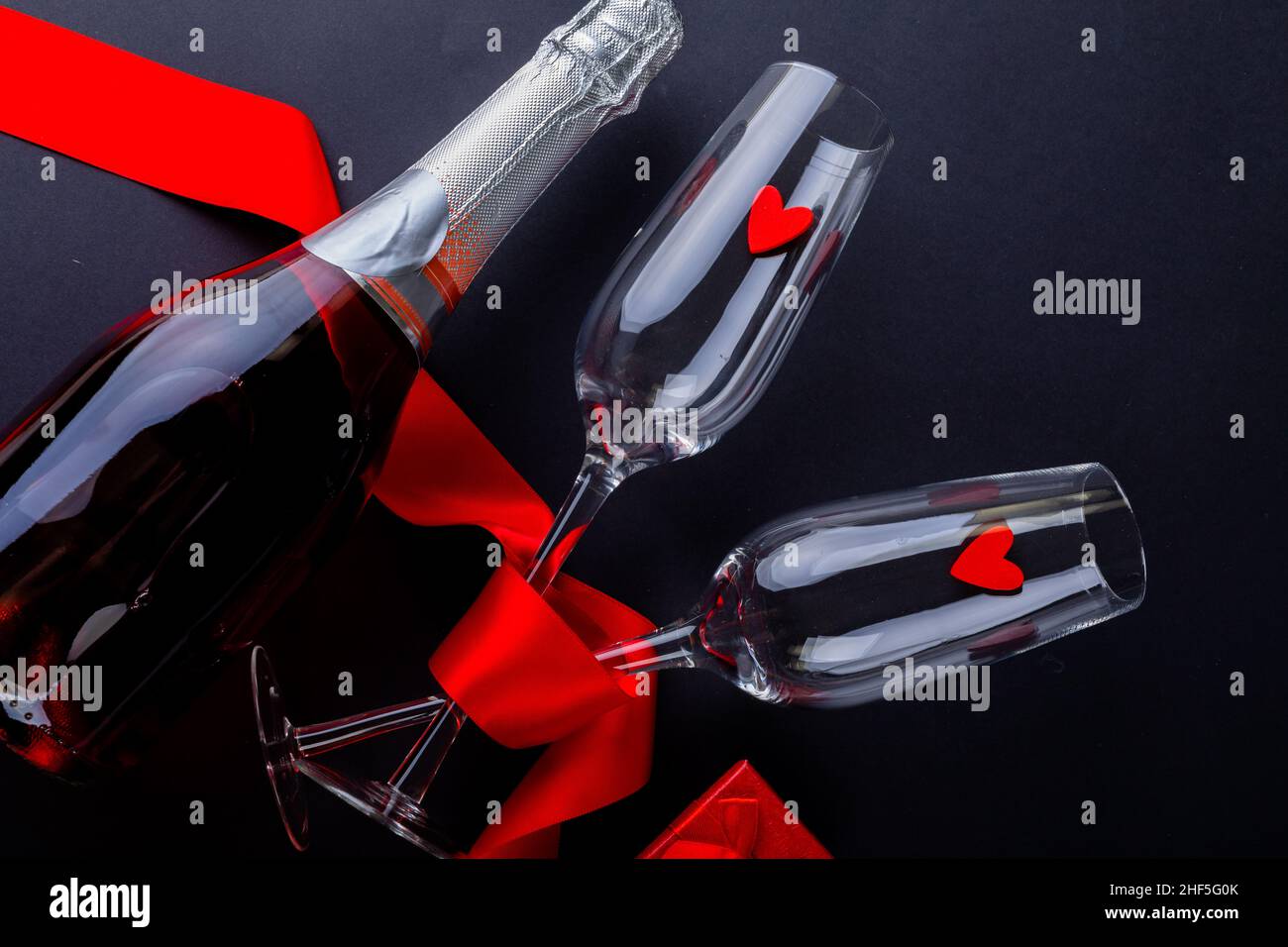 Herzformen in Flöten mit rotem Band von Champagnerflasche auf schwarzem Hintergrund mit Kopierraum Stockfoto