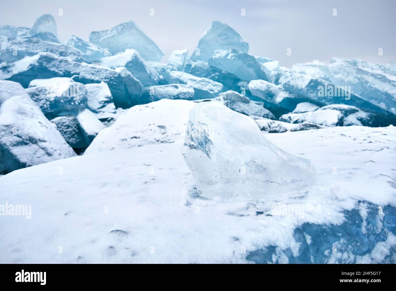 Schöne Landschaft aus kleinem Stück transparentem Eis am Bummock und Rissen am gefrorenen See mit Schnee. Naturkalender im Freien Stockfoto