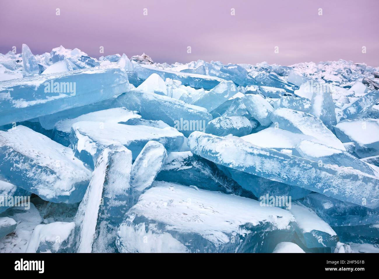 Wunderschöne Landschaft mit großen blauen Peace of Ice-Hummock und Rissen am gefrorenen See mit purpurem Morgenhimmel Stockfoto