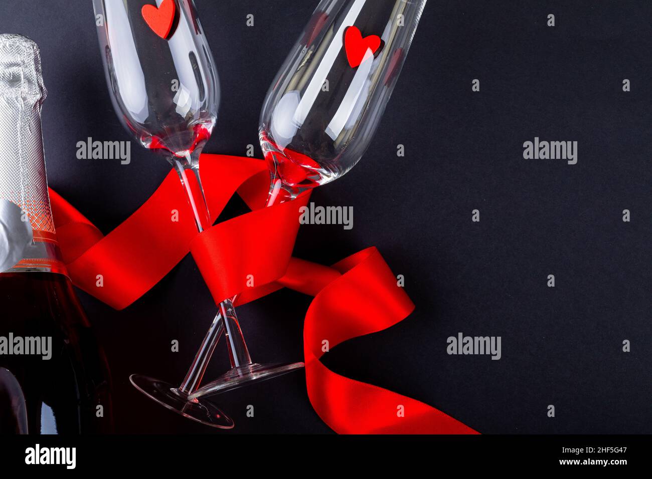 Rotes Band umhüllt Flöten mit Herzformen von Champagnerflasche und Kopierraum auf schwarzem Hintergrund Stockfoto