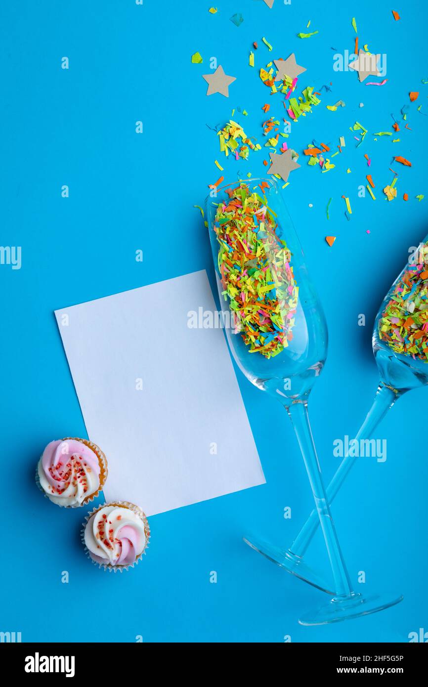 Sektflöten mit Konfetti von Cupcakes und leerem Papier mit Kopierfläche auf blauem Hintergrund Stockfoto