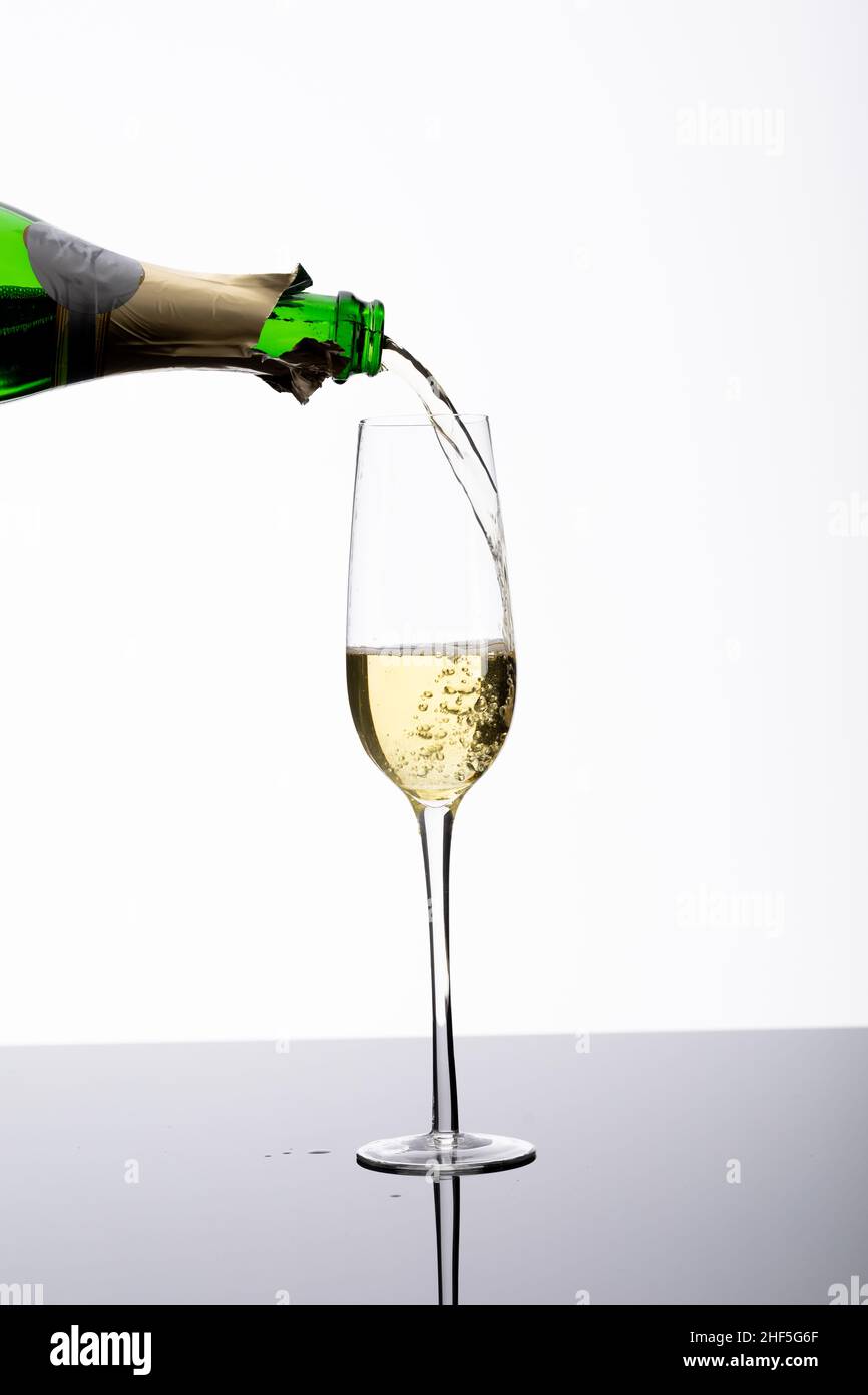 Nahaufnahme einer Flasche, die Champagner in Flöte auf den Tisch vor weißem Hintergrund mit Kopierfläche gießt Stockfoto