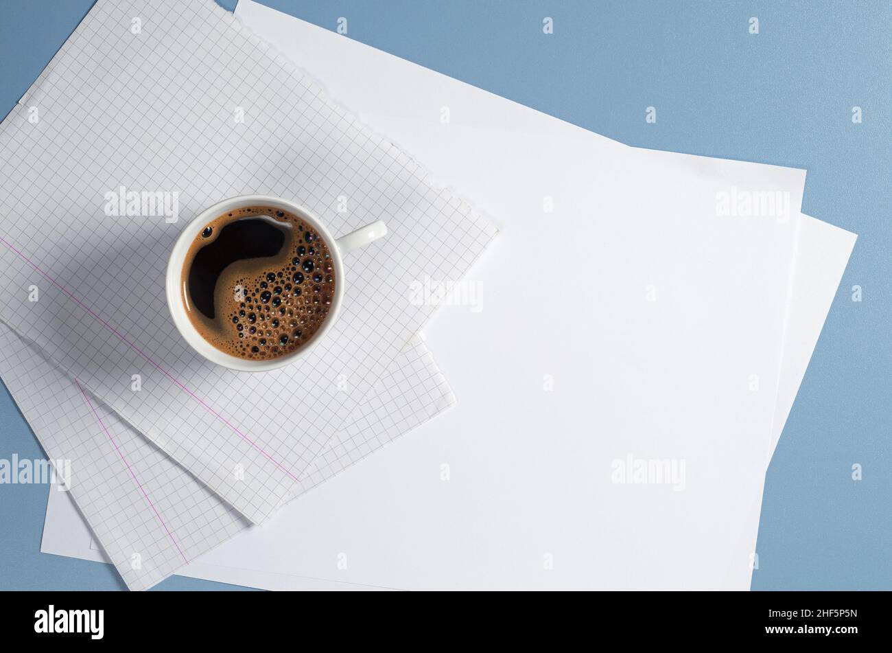 Tasse Kaffee und saubere weiße Papierblätter auf blauem Schreibtisch, Draufsicht mit Platz für Kopien Stockfoto