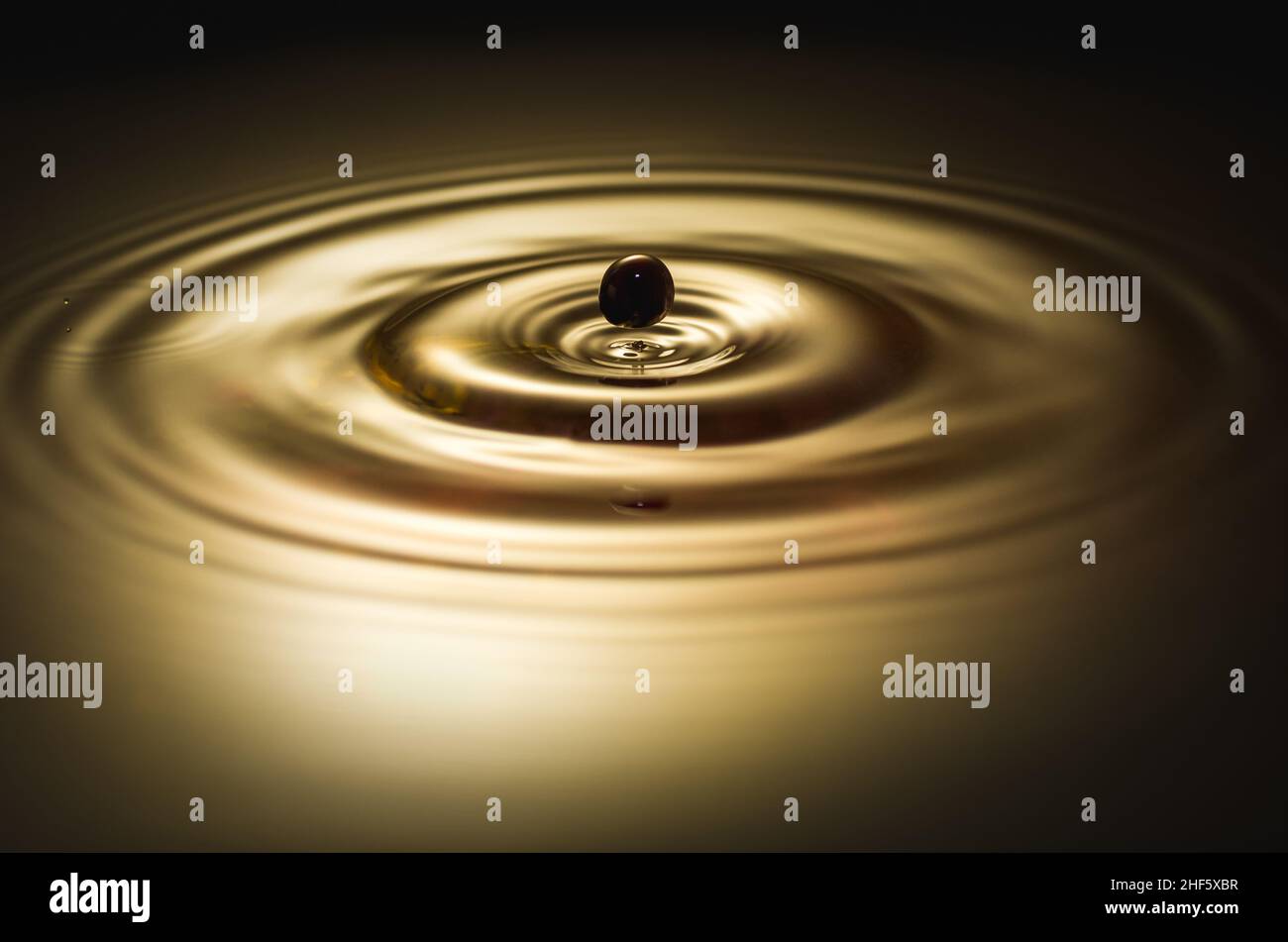 Schwarzer Tropfen fällt ins Wasser und erzeugt Kreise Stockfoto