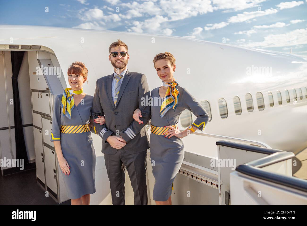 Ein Flugkapitän und zwei Flugbegleiterinnen schauten in der Nähe der Flugzeugtüren lächelnd auf die Kamera Stockfoto
