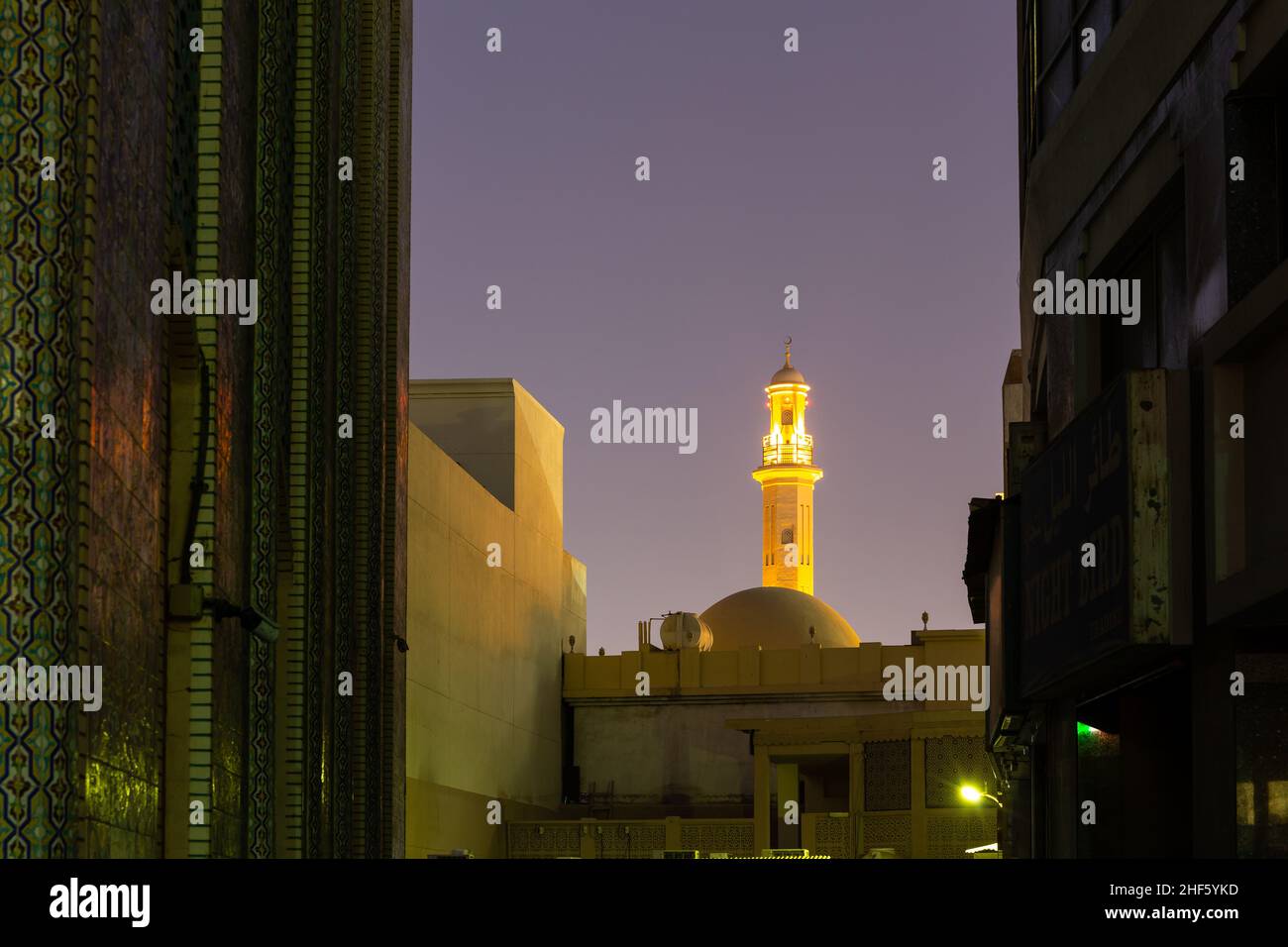 Beleuchtete Minarett der Großen Moschee in Dubai (Grand Bur Dubai Masjid) bei Nacht, zwischen den Gebäuden von Bur Dubai, Vereinigte Arabische Emirate gesehen. Stockfoto