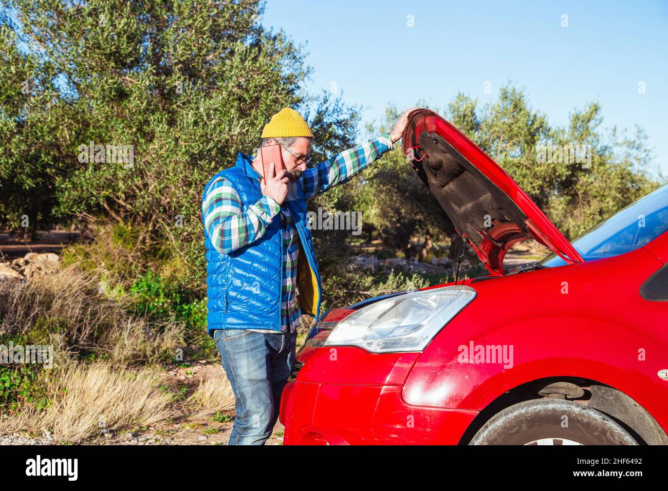 Bärtiger Mann, der auf der Straße neben seinem heruntergekommenen Auto telefonierte Stockfoto