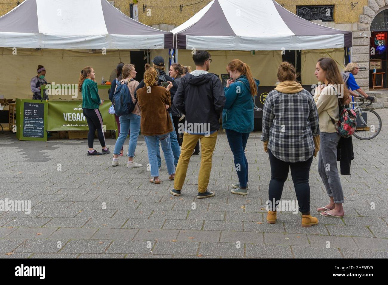 Junge Leute, die an einem veganen Imbissstand auf einem Straßenmarkt in Falmouth in Cornwall auf Essen warren. Stockfoto