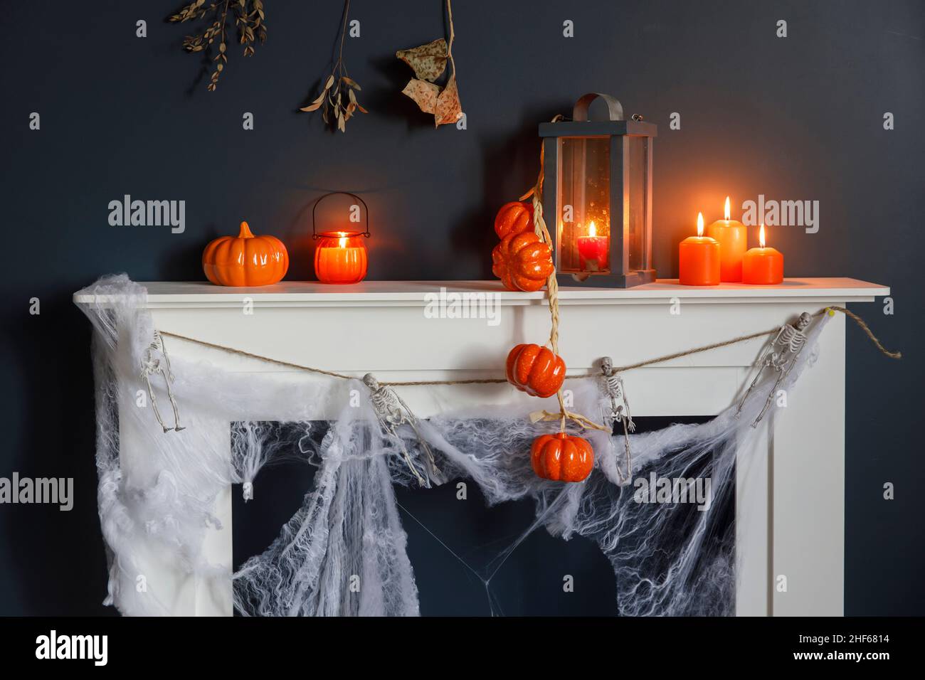 Halloween-Heimtextilien. Plastikspielzeug-Skelette in einer Holzkiste am Kamin vor einer dunkelblauen Wand. Eine Girlande aus Skeletten. Spinnennetz auf den dres Stockfoto