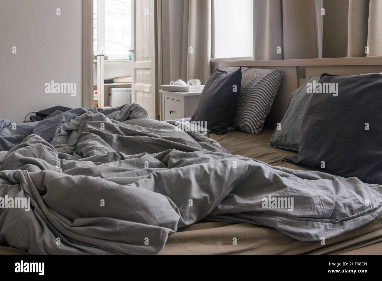 Ein ungemachtes Bett mit zwei Daunendecken in grauer Bettdecke. Morgenkonzept Stockfoto