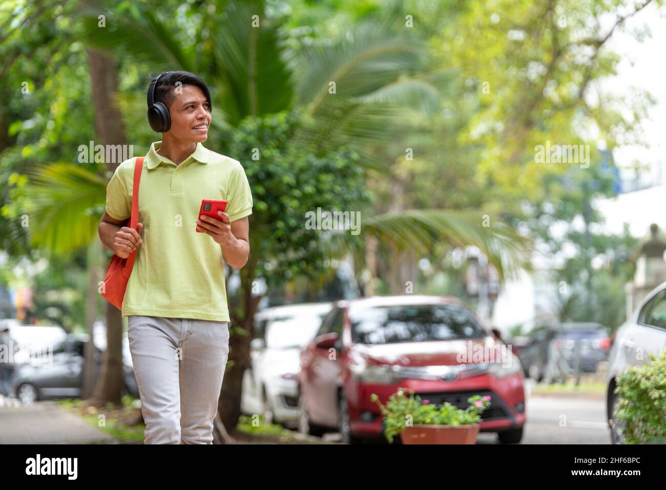 Ein junger Latino-Mann, der mit dem Telefon in der Hand die Straße entlang läuft Stockfoto