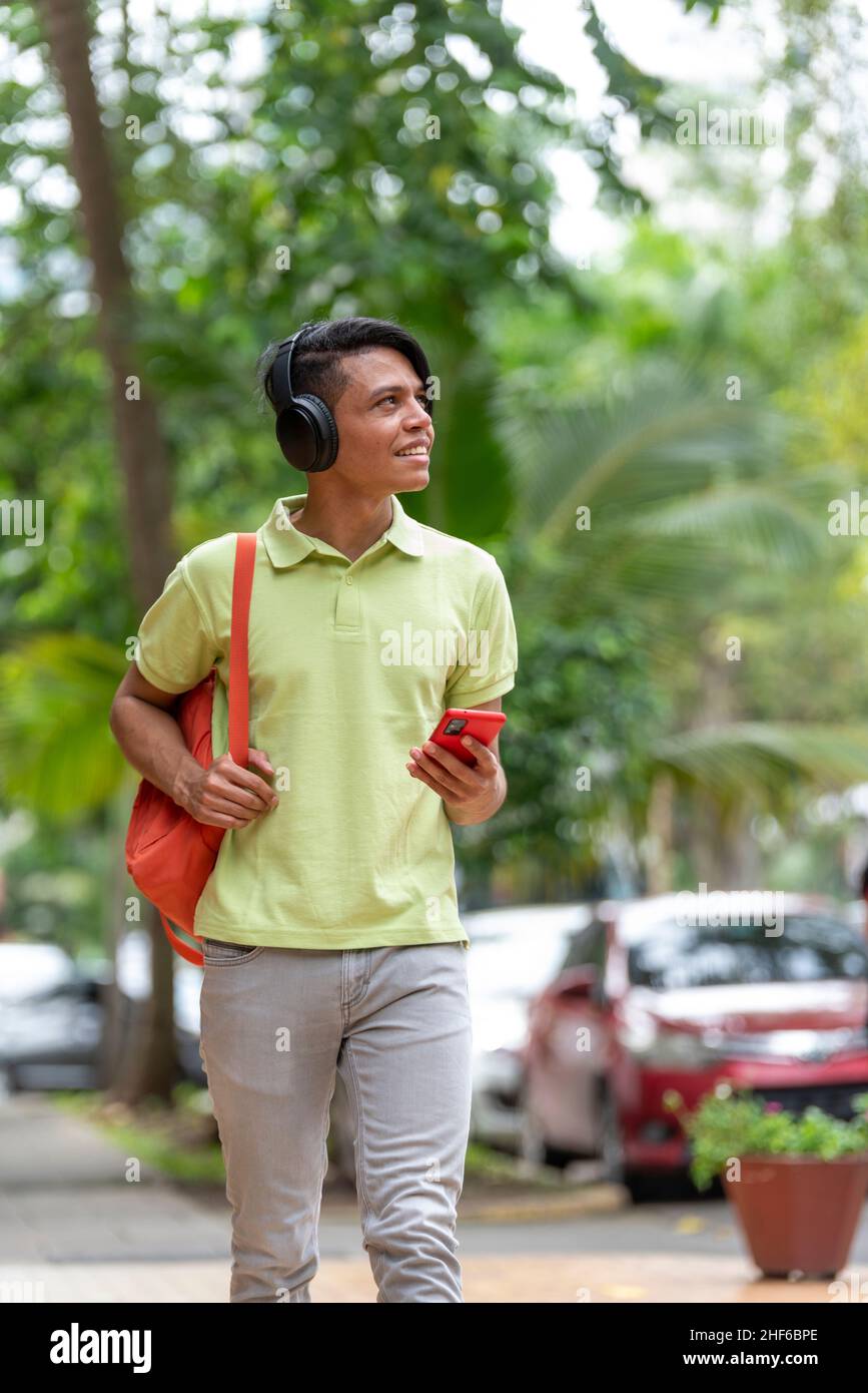 Ein junger Latino-Mann, der mit dem Telefon in der Hand die Straße entlang läuft Stockfoto