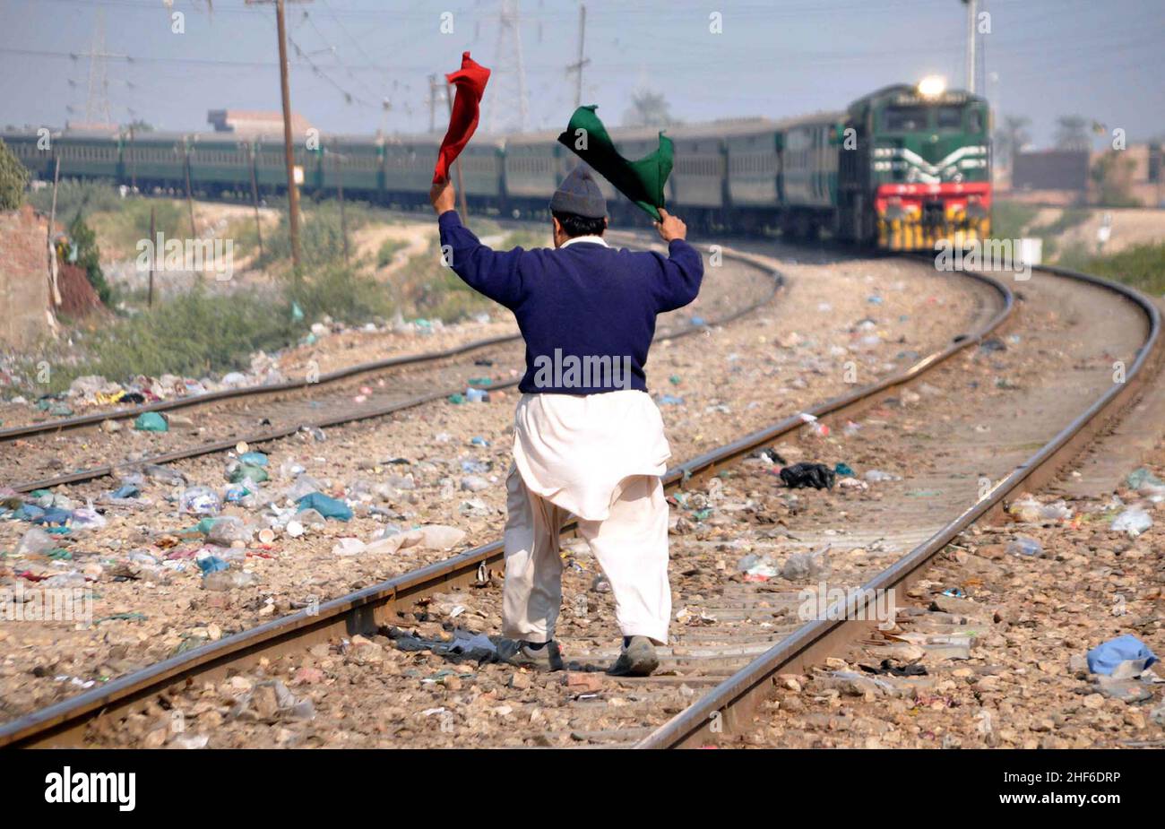 Eisenbahntor-Mann zeigt Flagge zum Zug, um aus unbekannten Gründen am Tando Yousaf Railway Crossing in Hyderabad am Freitag, 14. Januar 2022, zu stoppen. Stockfoto