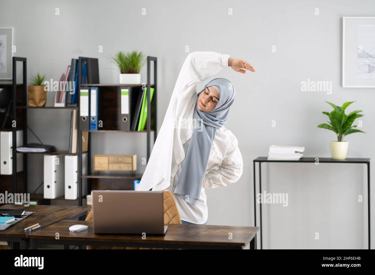 Frau In Hijab Steht Und Dehnt Sich Vor Dem Computer Stockfoto