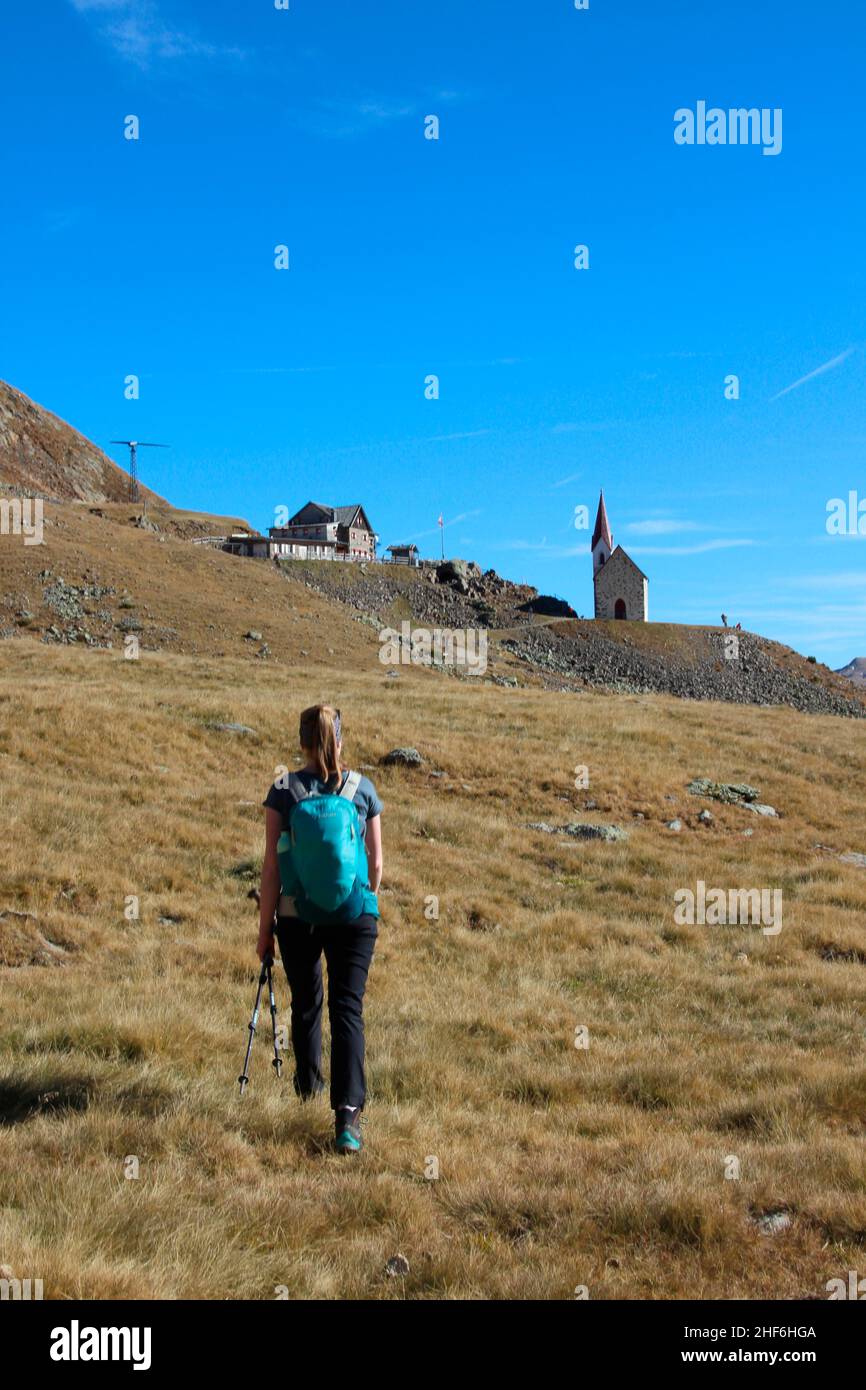 Junge Frau auf Wanderung. Latzfons, Klausen, Provinz Bozen, Südtirol, Italien, Europa. Die Wallfahrtskirche und die Wallfahrtskirche des Latzfonser Kreuzes unter einem klaren blauen Himmel Stockfoto