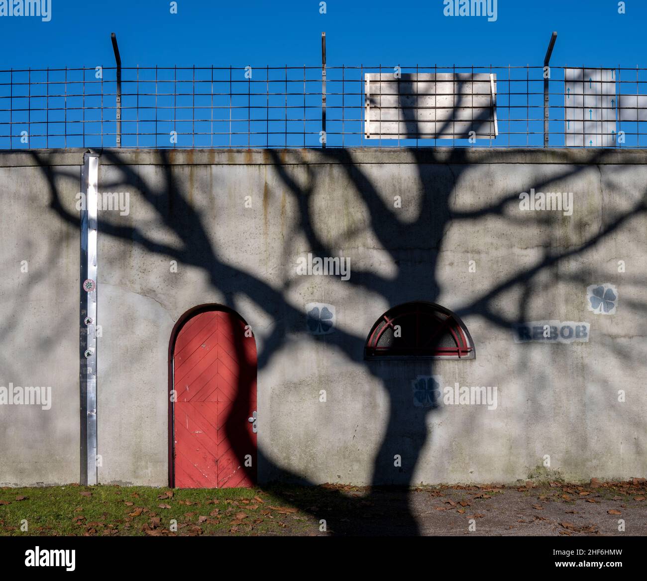 Schatten, Mauer, rotes Tor, blauer Himmel, rot-weißes Oberhausen Stockfoto