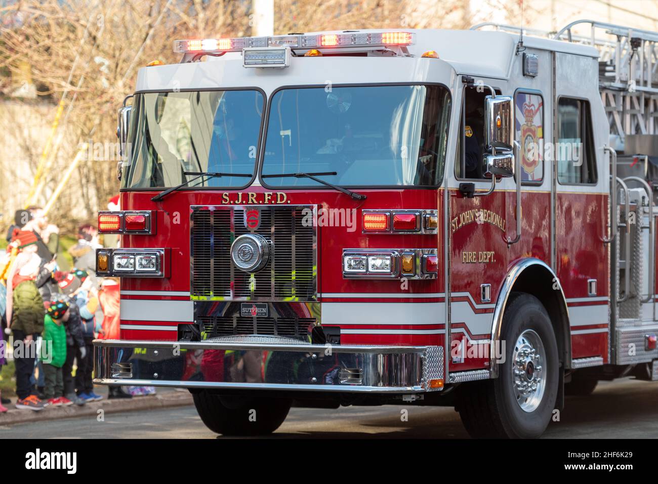 Ein großer rot-weißer Feuerwehrwagen von der St. John's Regional Fire Station fährt eine kleine Straße entlang mit Menschen auf der Beifahrerseite des Fahrzeugs Stockfoto