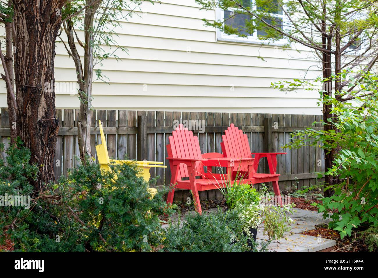 Das Äußere einer alten weißen Cape Cod horizontalen Klapptafel Holzbrett Stil Abstellwand mit doppelt hängenden Fenstern.Es gibt einen weißen Adirondack Stuhl Stockfoto