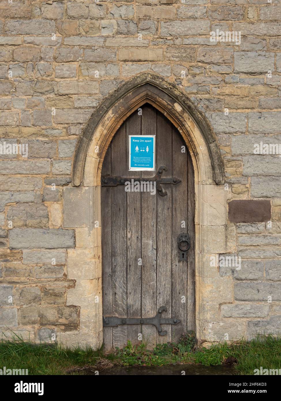 Traditionelle Kirchentür mit modernem Covid 19 Sozialabweichendes Zeichen. St Andrew's Church, Burnham-on-Sea, Somerset Stockfoto