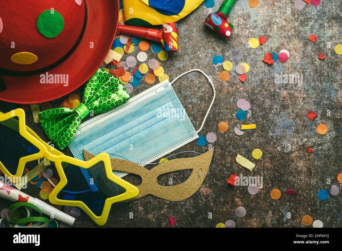 Konzept des Karnevals während des Covid-19. Draufsicht auf Accessoires für Karneval mit schützender OP-Maske über grunge-Hintergrund. Karnevalsfeier c Stockfoto