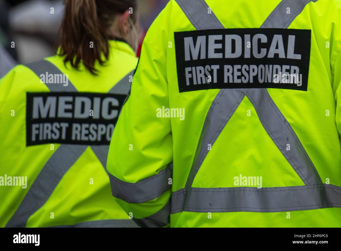 Medizinische Ersthelfer, die mit schwarzen Wollstoppkappen und gelben reflektierenden Mänteln auf einer Straße unterwegs sind, mit dem medizinischen Ersthelfer in Grau. Stockfoto