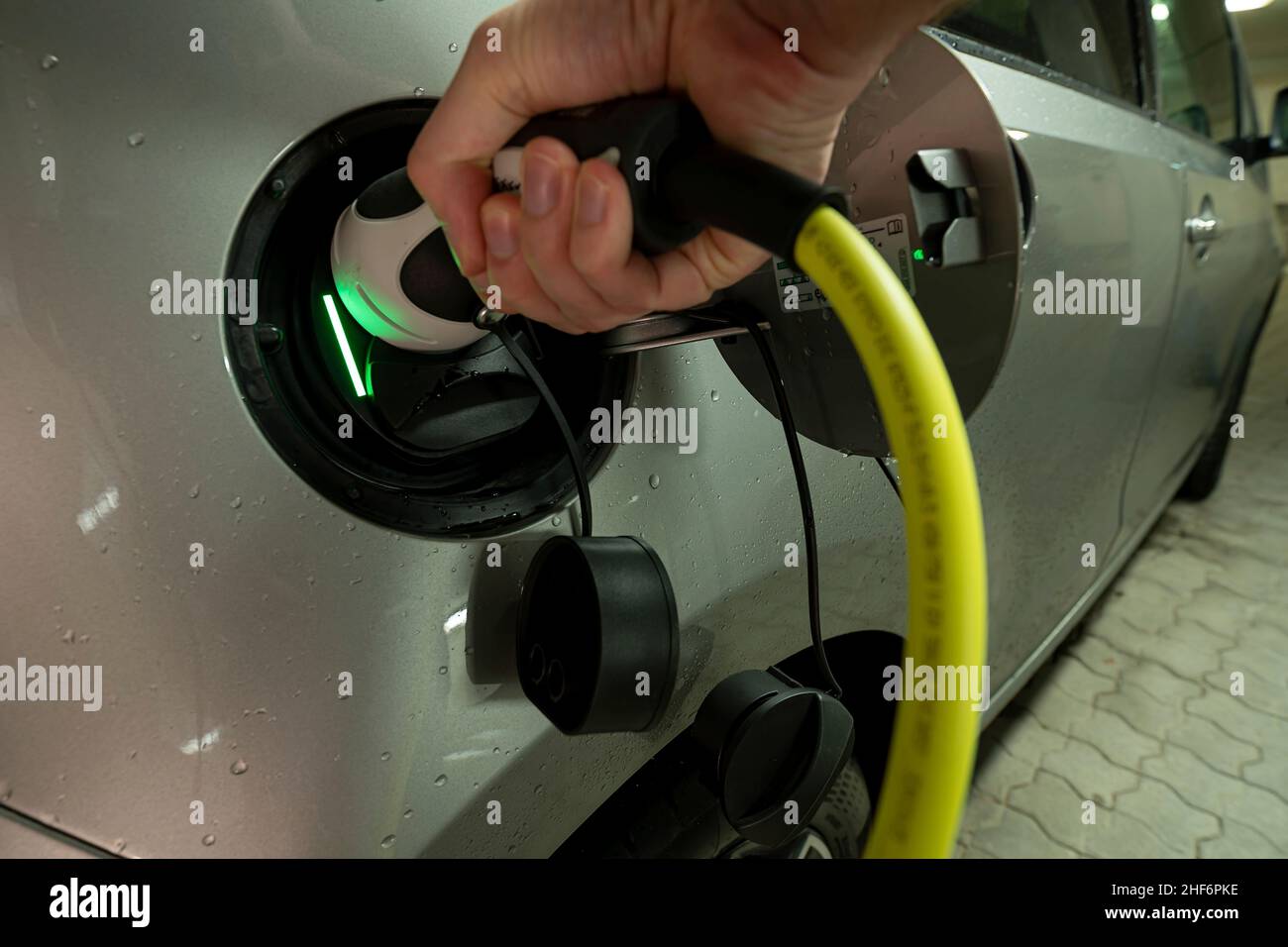 Hände auf das Ladekabel eines E-Autos mit aktivem Ladevorgang, das durch das grüne Licht angezeigt wird Stockfoto