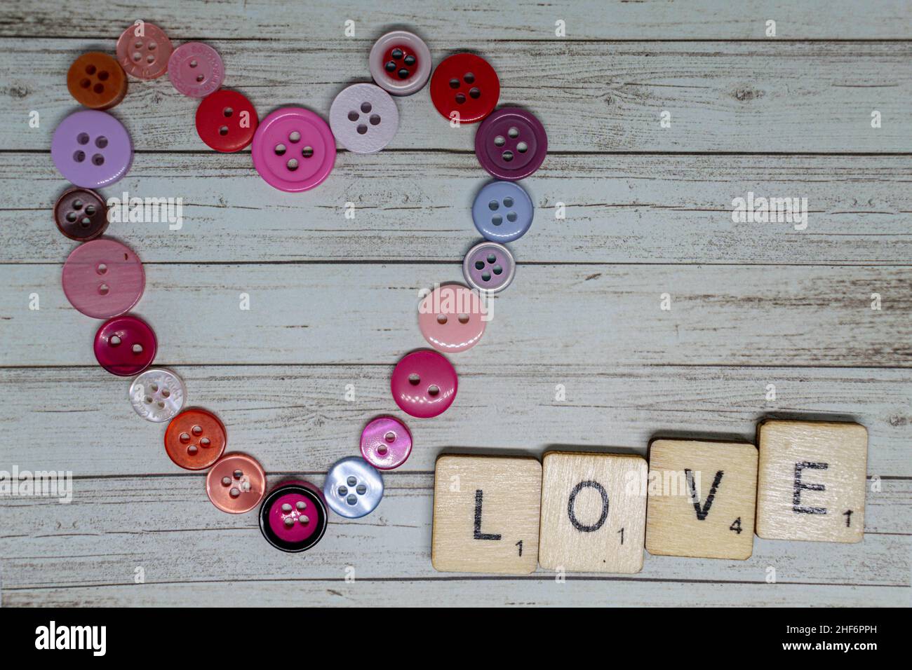 Liebe und Romantik Konzept. Love Heart Form aus rosa und roten Knöpfen mit scrabble spielen Würfel Rechtschreibung Love You. Romantischer Valentinstag Stockfoto