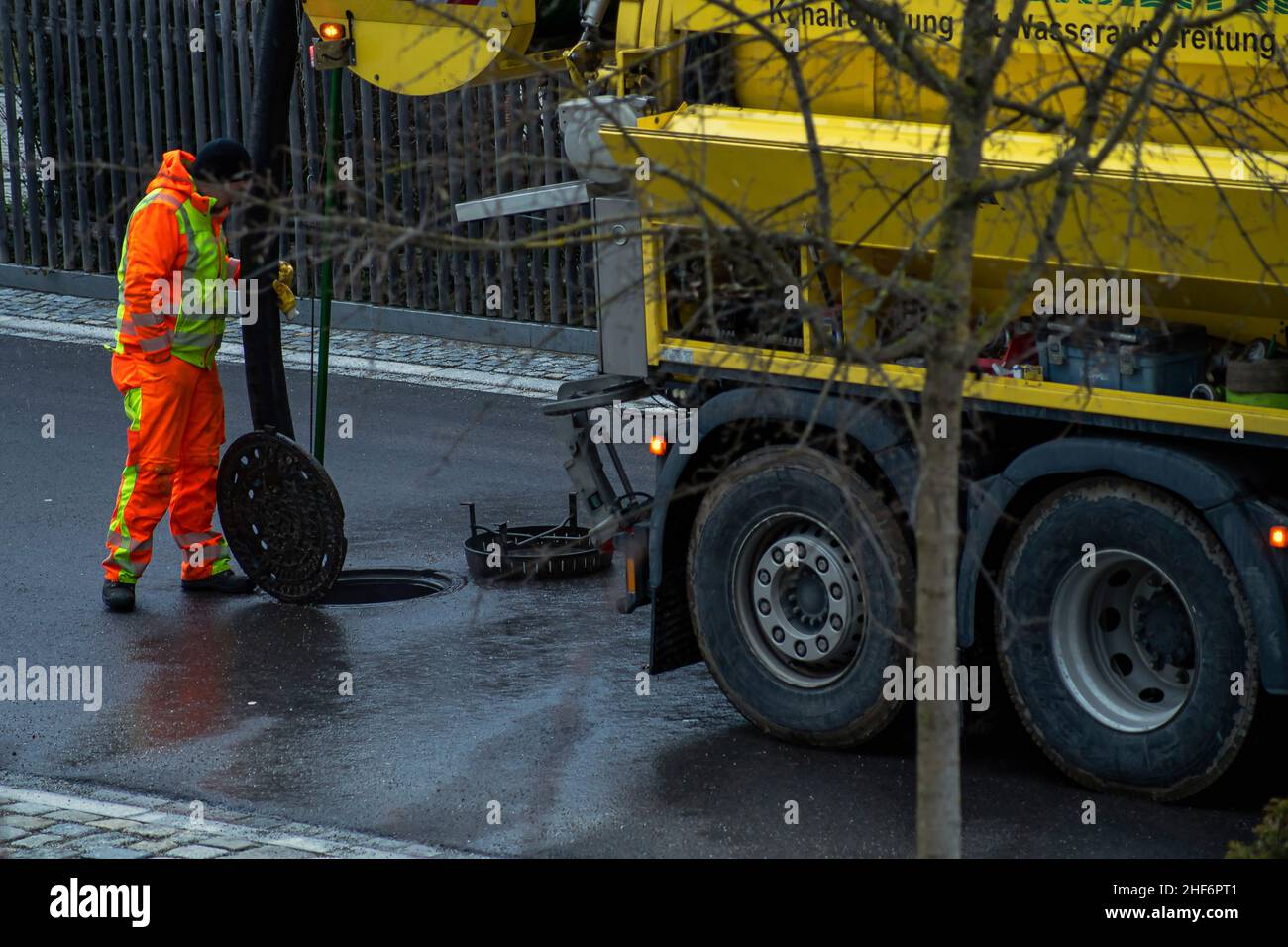 Arbeitskanal-Bagger, der die Arbeit an einem offenen Schachtloch auf einer nassen Straße an der Rückseite des Kanalreinigungsfahrzeugs ausführt Stockfoto